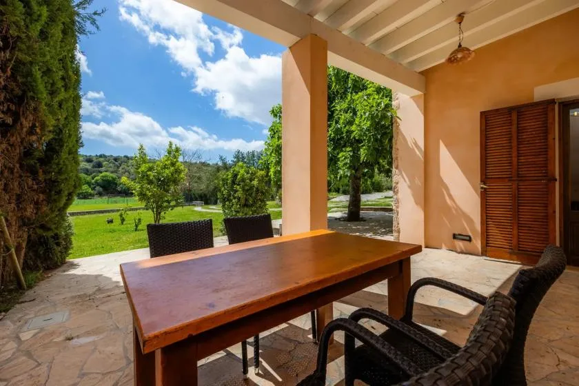 Una zona de comedor exterior cubierta con una mesa de madera junto a un jardín verde.