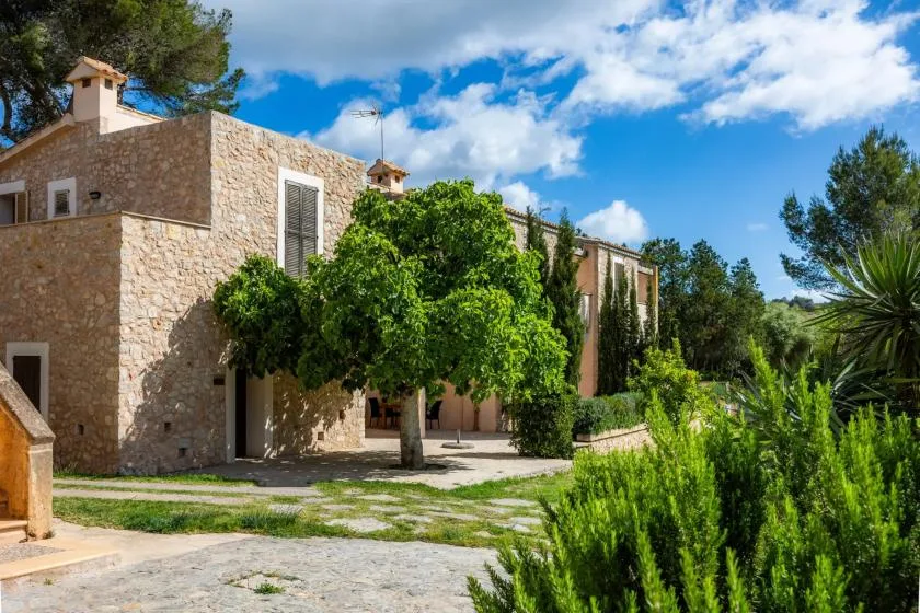 Un edificio de piedra se encuentra entre árboles y vegetación bajo un cielo parcialmente nublado.