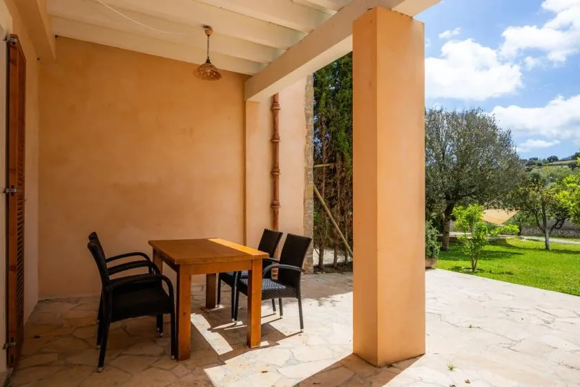 A covered outdoor dining area with a wooden table and chairs overlooks a green garden.