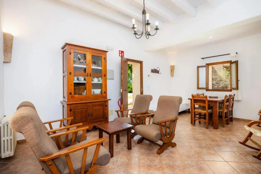 Zona de comedor y estar con asientos de madera, una mesa y un armario con puertas de vidrio.