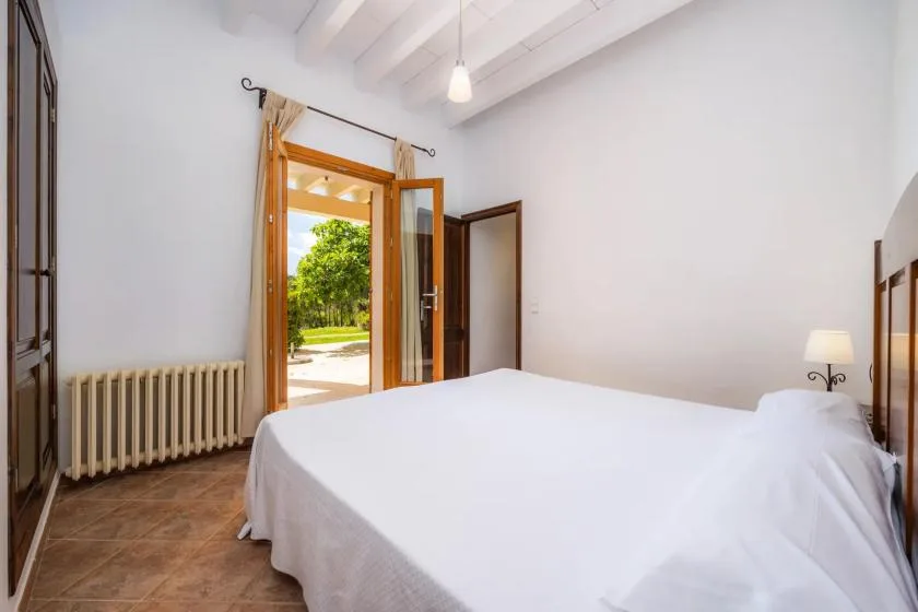 Dormitorio con una cama blanca junto a puertas abiertas que dan al exterior.
