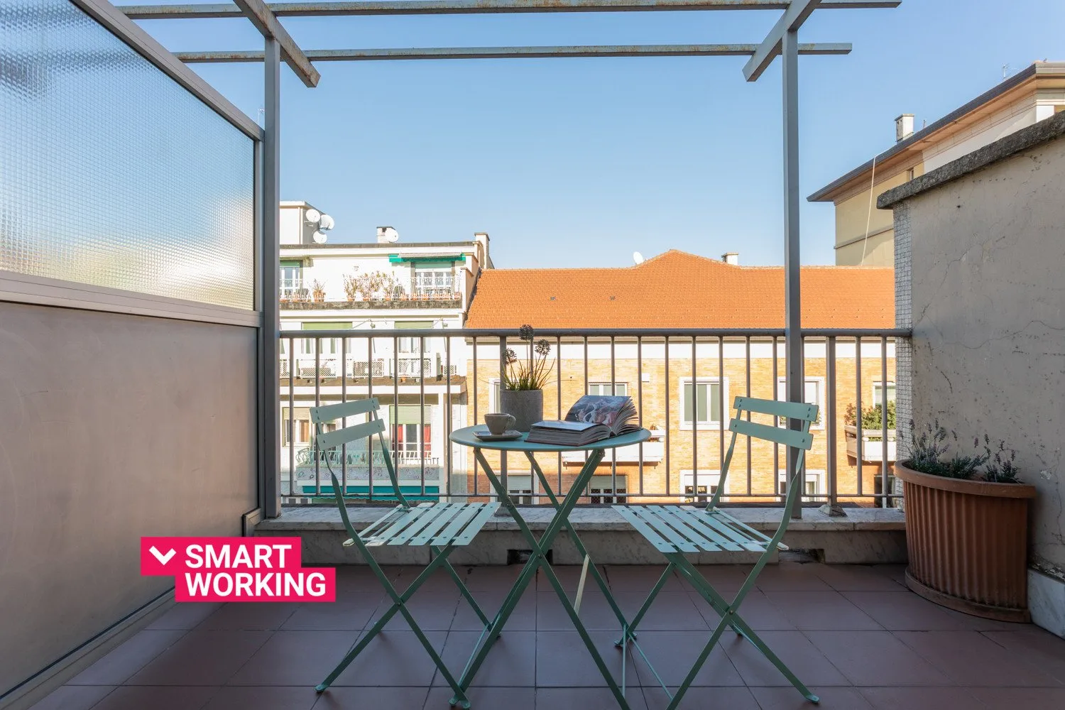 A balcony with outdoor seating and a small table overlooks nearby buildings.