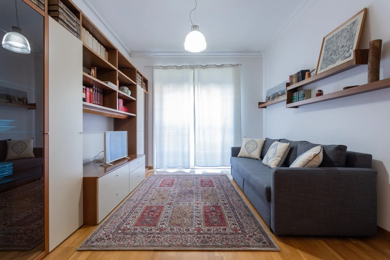 Una sala de estar con un sofá oscuro, estanterías y una alfombra estampada.