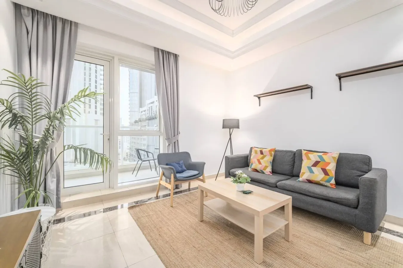 Una sala luminosa con asientos grises, una mesa de centro y ventanas grandes.