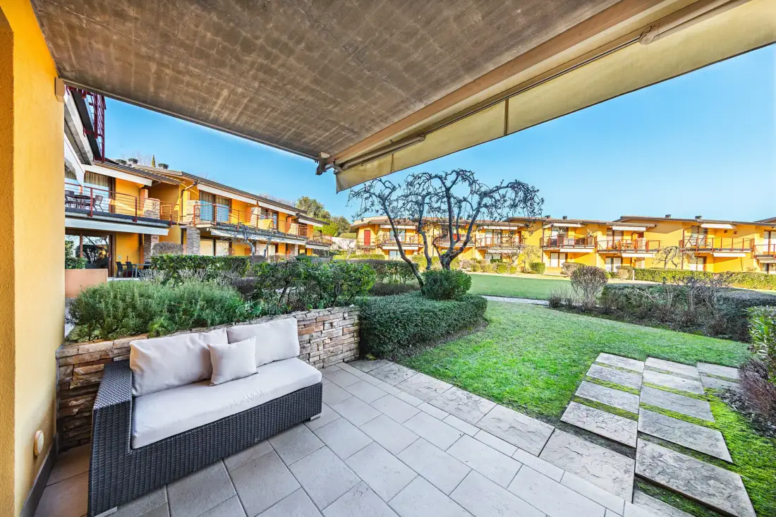 A covered patio overlooks a landscaped courtyard with lawn and seating.