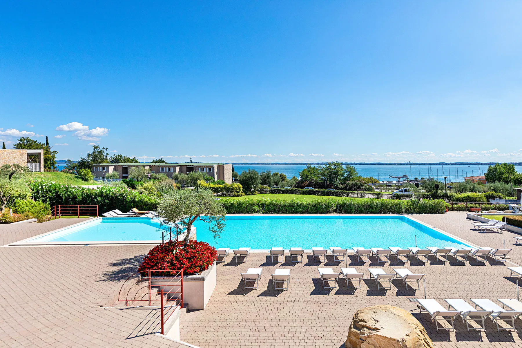 An outdoor swimming pool is surrounded by paved decking and rows of loungers.