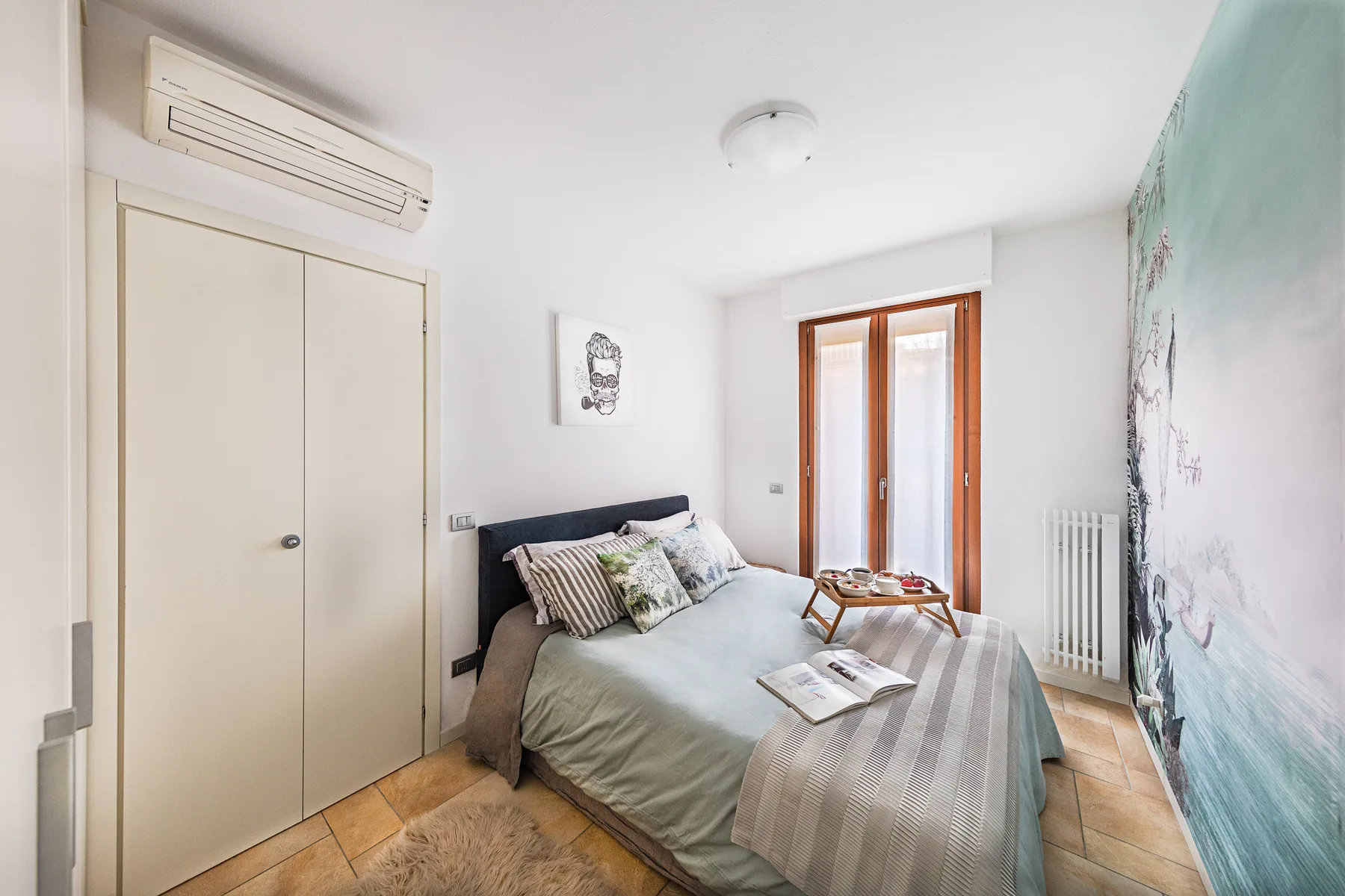 A bright bedroom with a bed beside tall glazed doors.