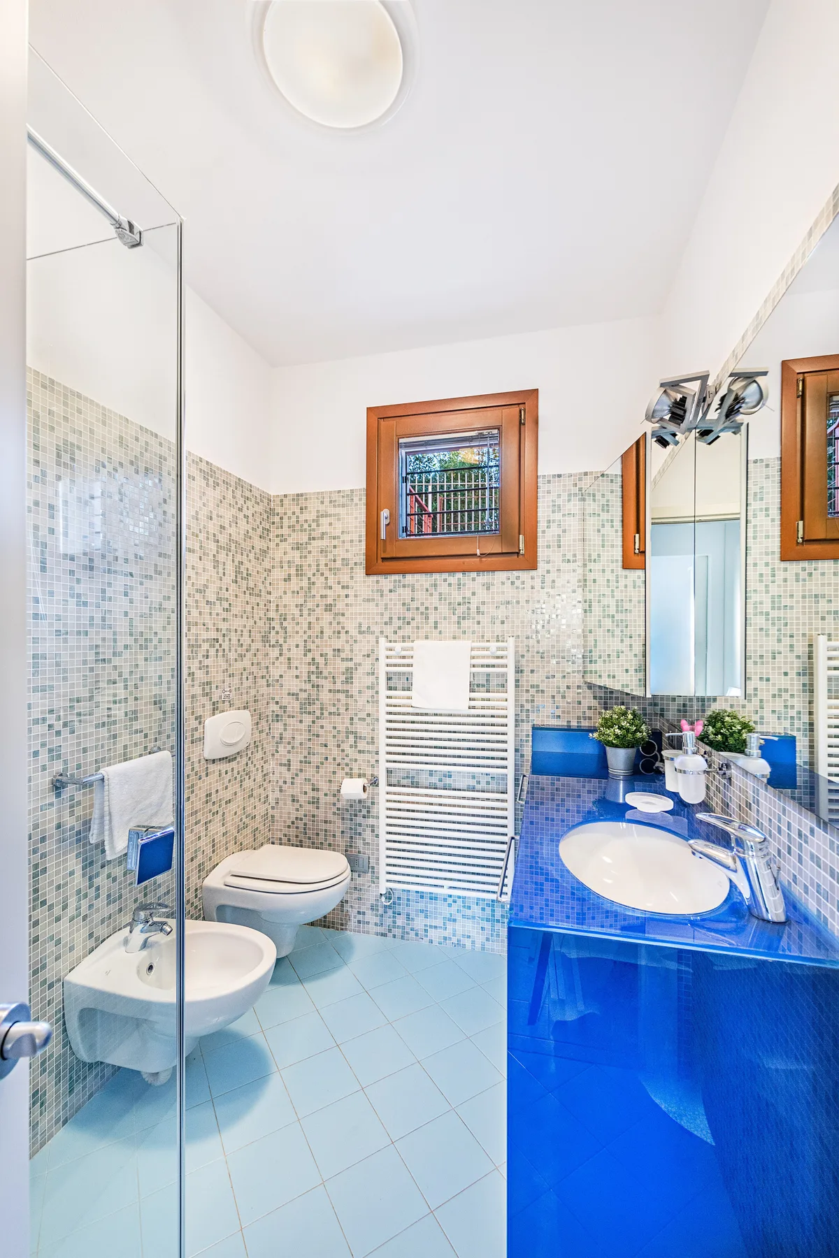 A tiled bathroom with a glass shower, toilet, and blue vanity.