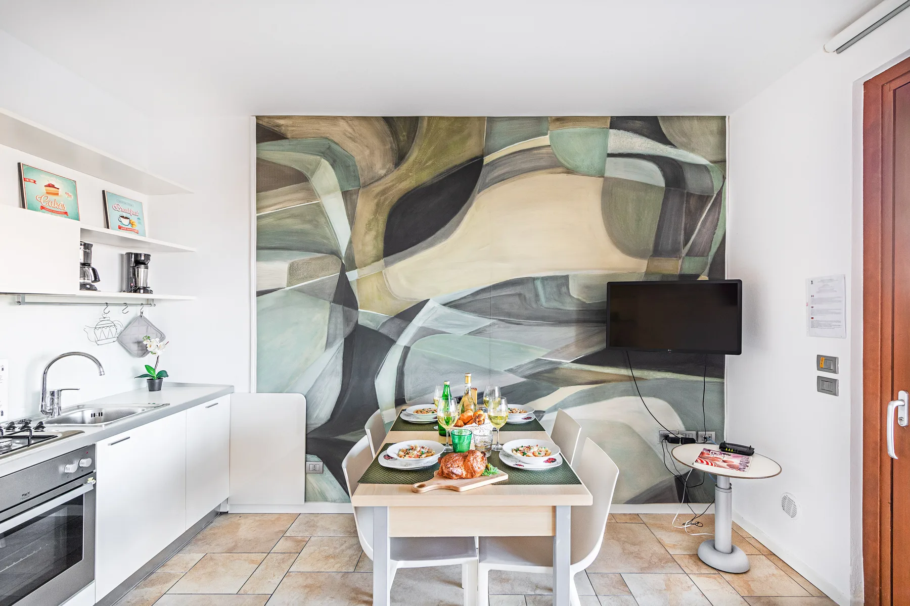 A dining area with a set table, kitchen counter, and large abstract wall mural.