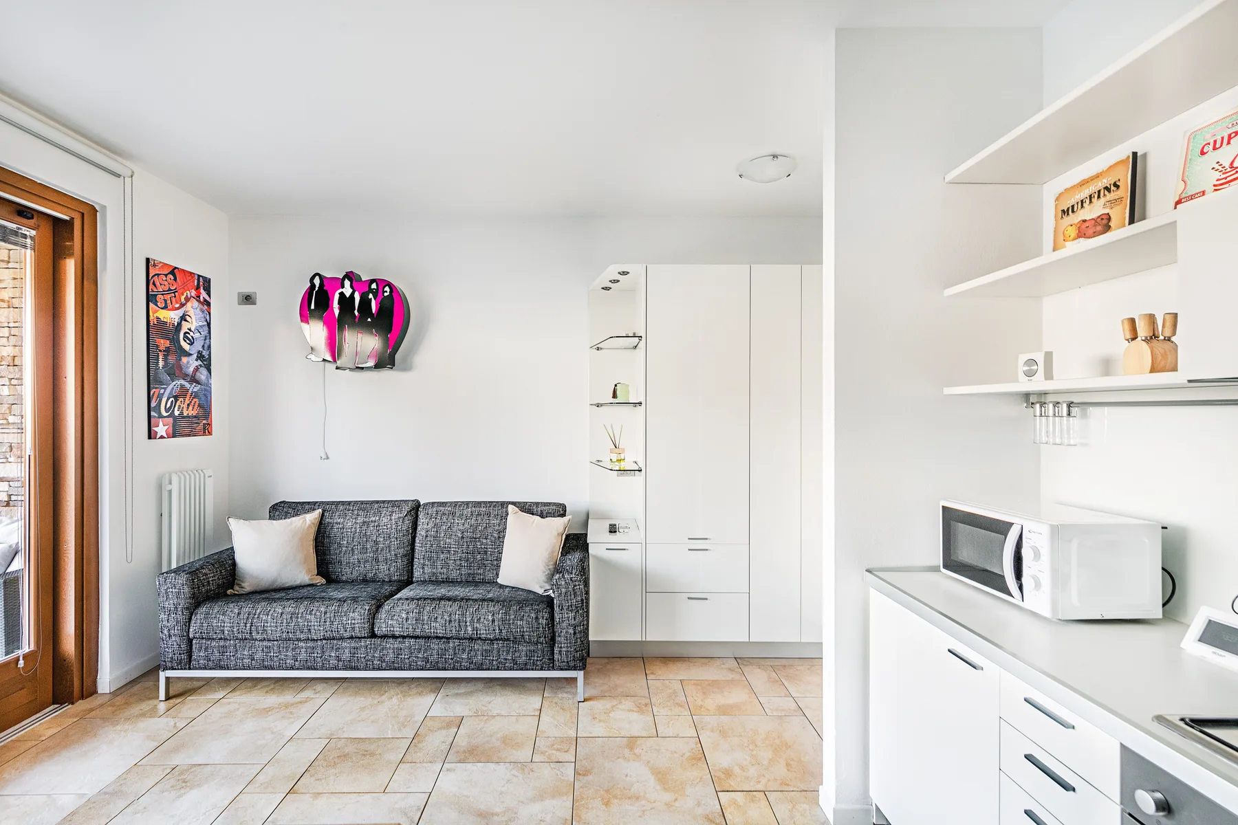 A bright living area with a gray sofa beside a white kitchenette.