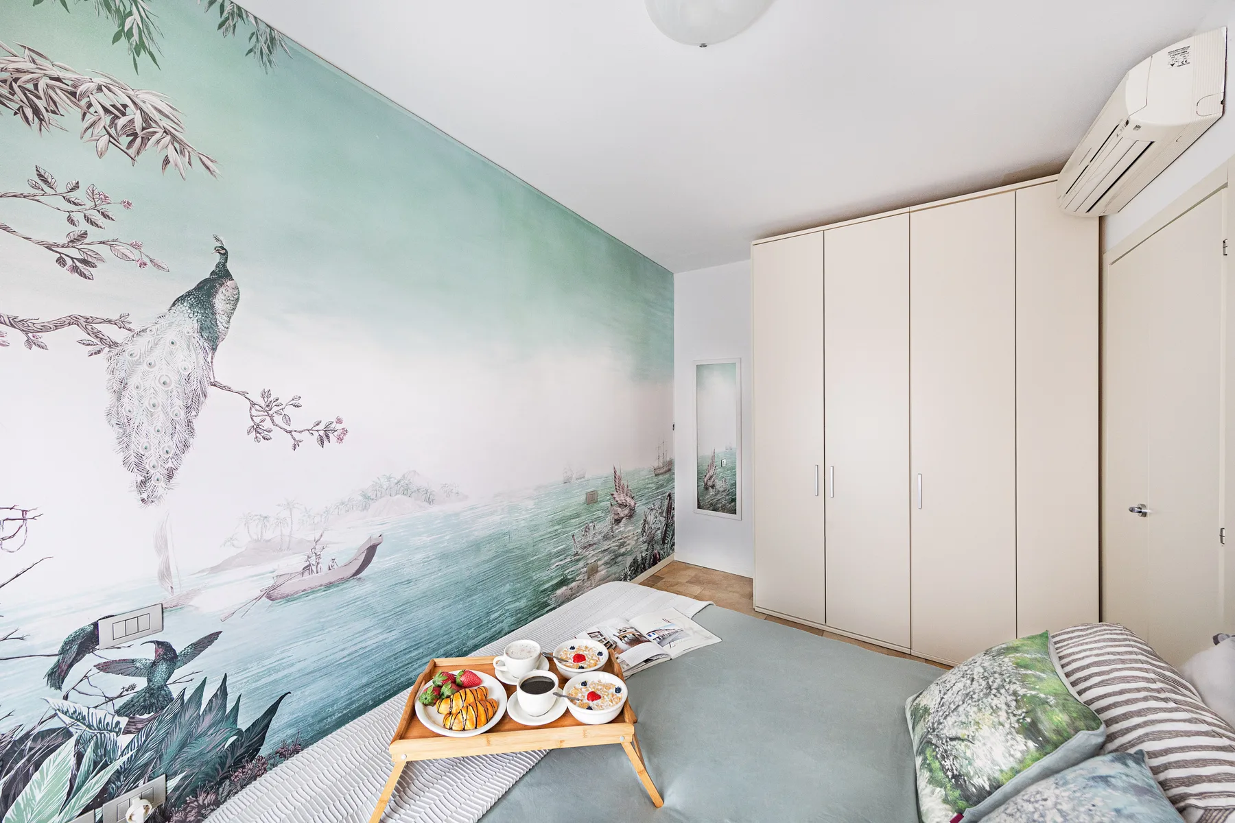 A bedroom with a large mural, built-in wardrobes, and a low table.
