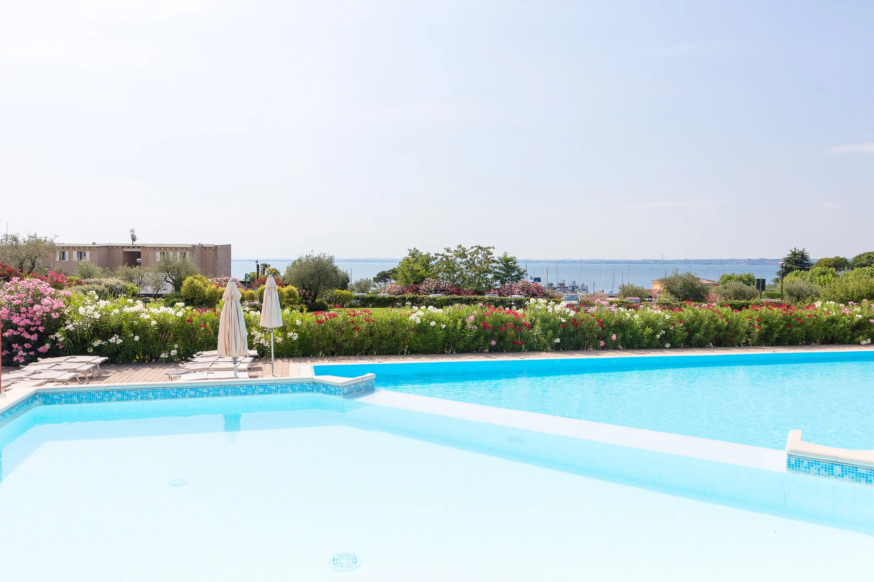 A swimming pool beside flowering gardens, with the sea visible in the distance.
