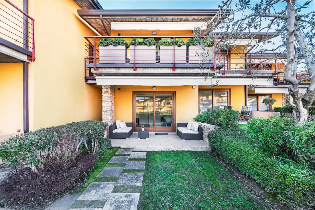 A landscaped courtyard with a stone path, hedges, and a building with balconies.