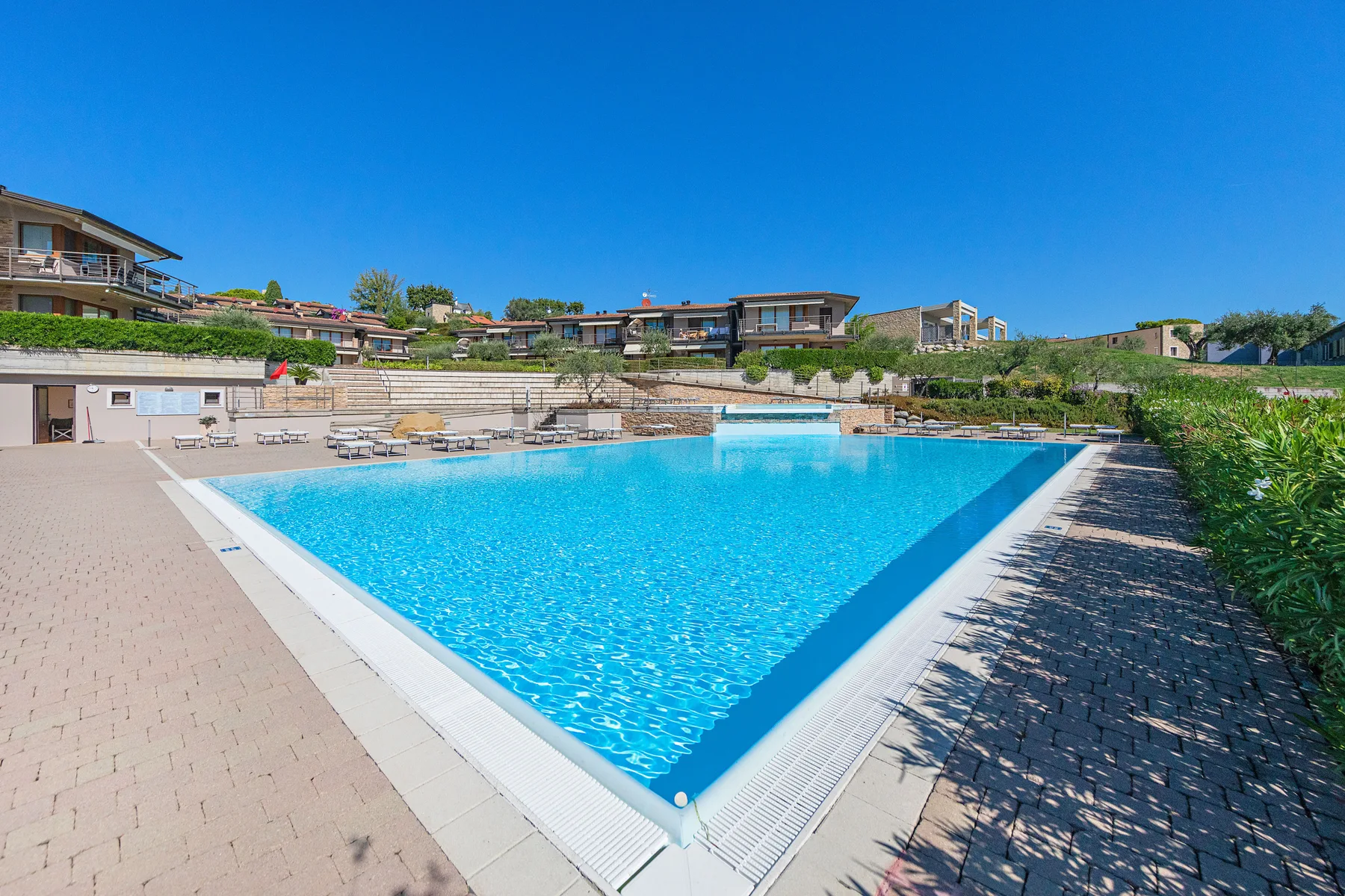 An outdoor swimming pool sits beside paved walkways and landscaped greenery.