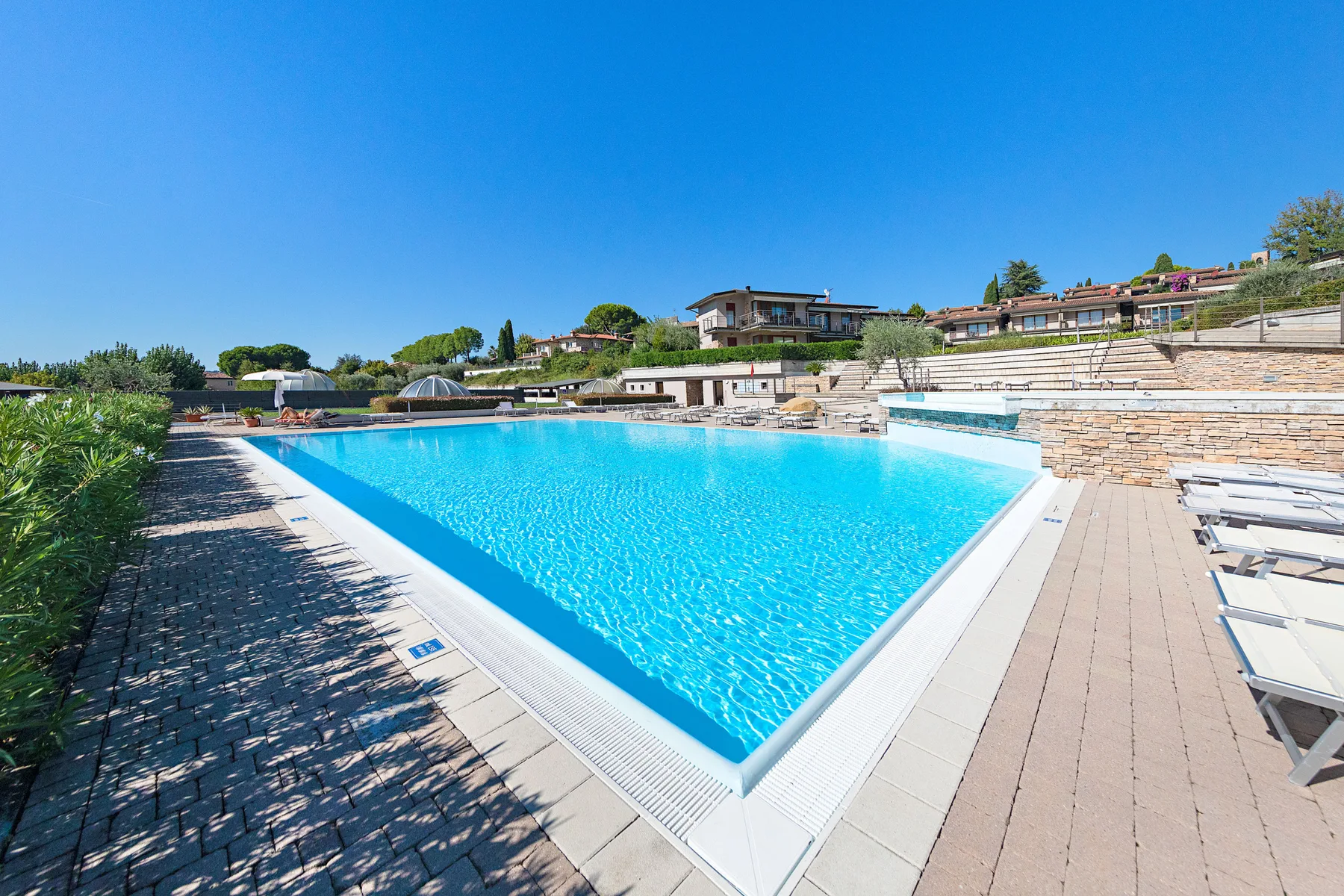 An outdoor swimming pool sits beside paved decking and landscaped grounds.