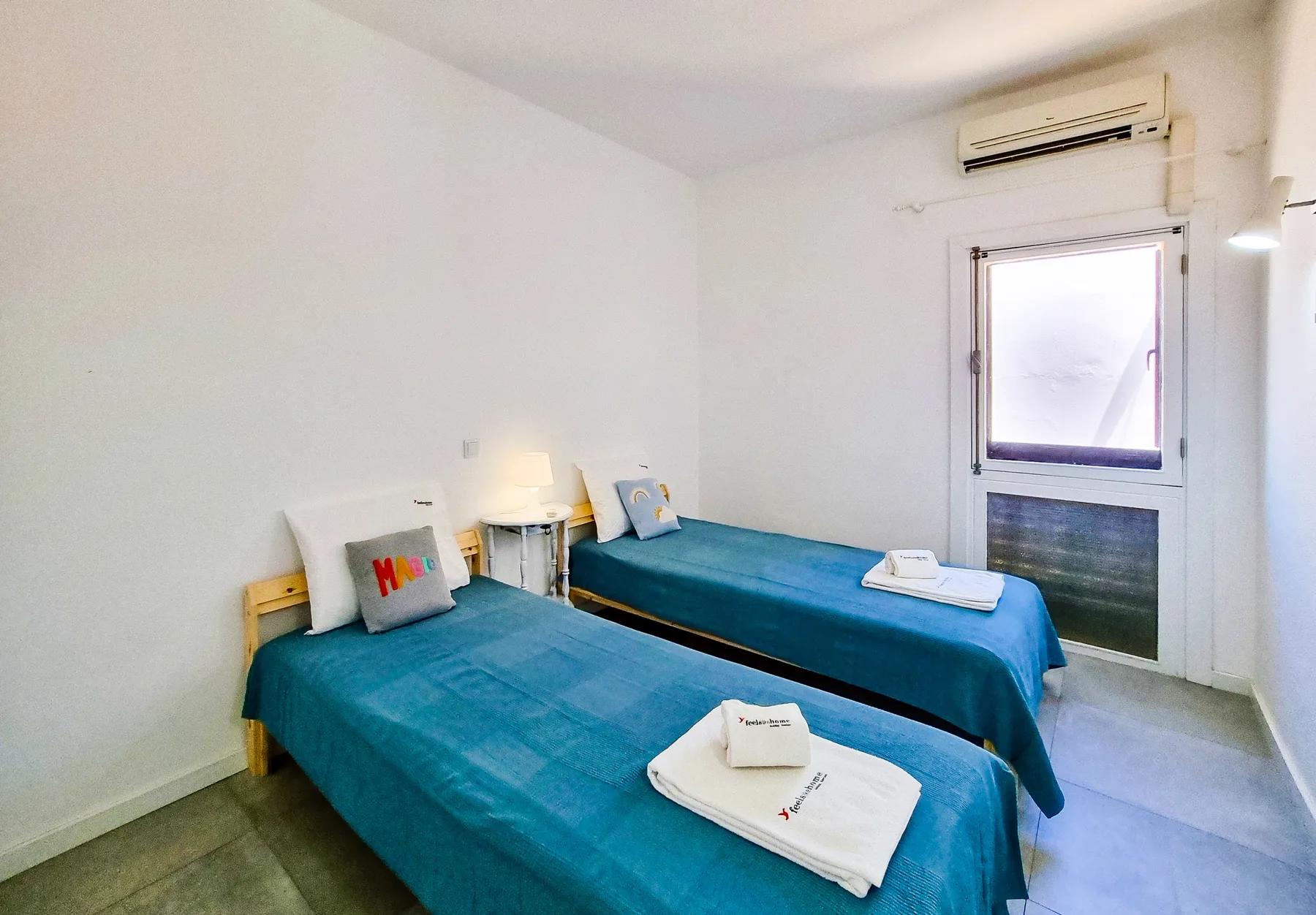 Dormitorio con dos camas, toallas dobladas y una pequeña mesa de noche.