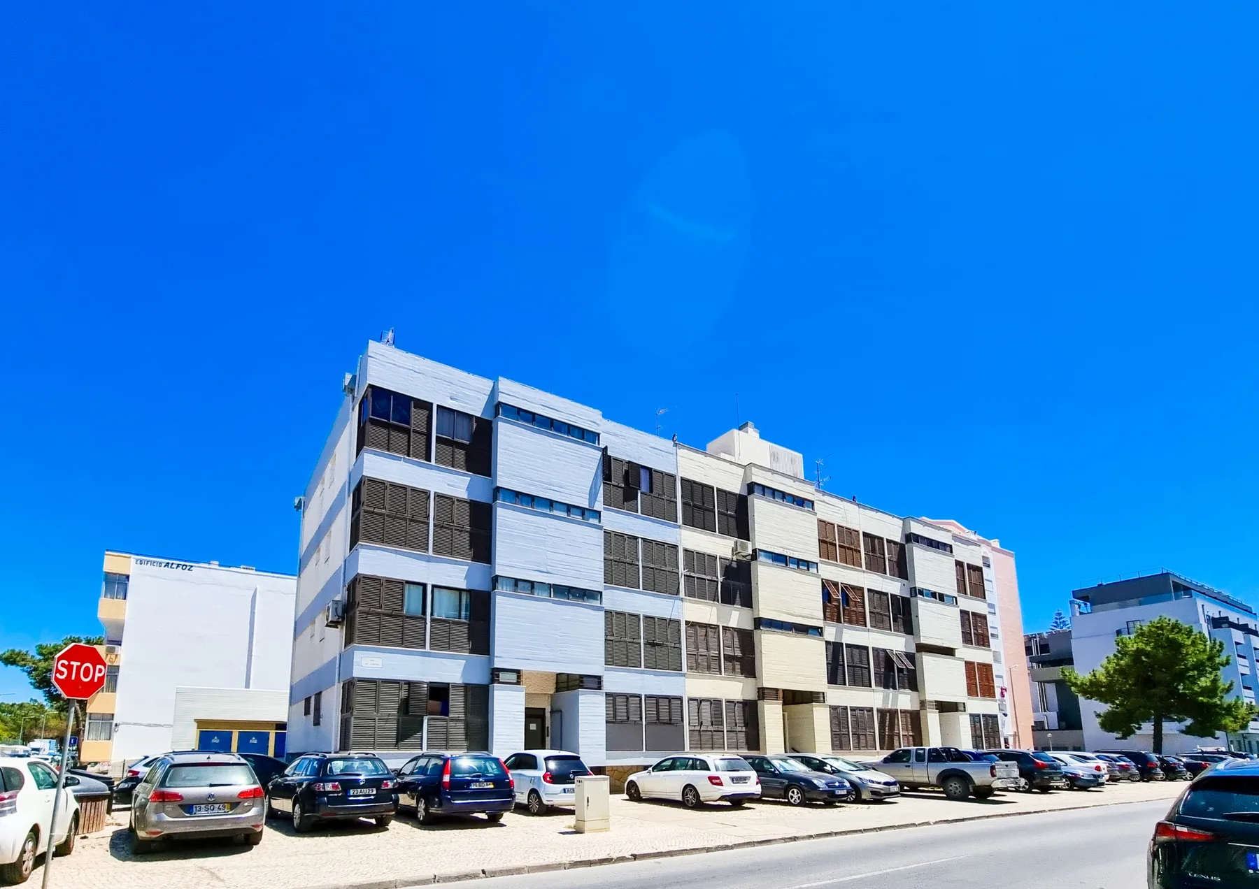 Un edificio de apartamentos de varias plantas está junto a una calle con coches estacionados.