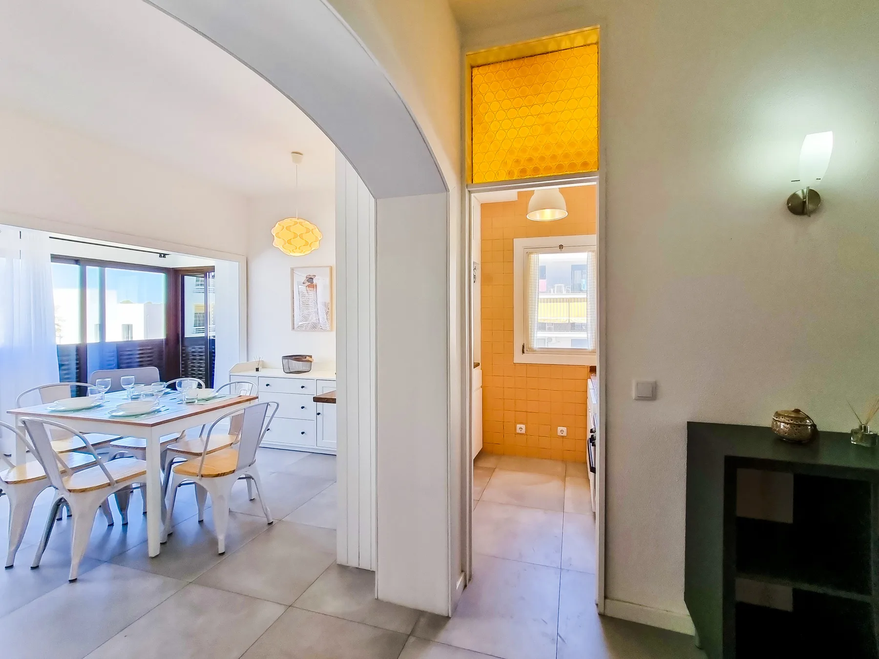 A bright dining area opens onto a kitchen and a small tiled room.