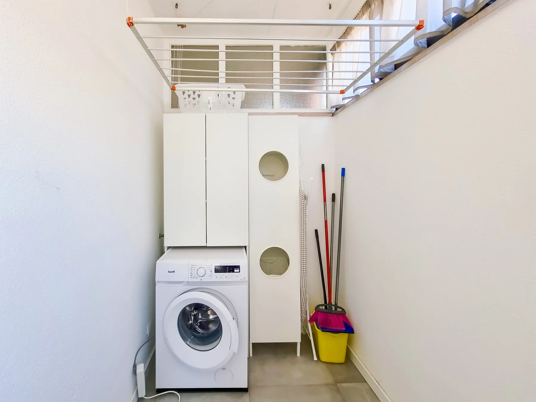 A laundry area with a front-loading washing machine and cleaning tools.