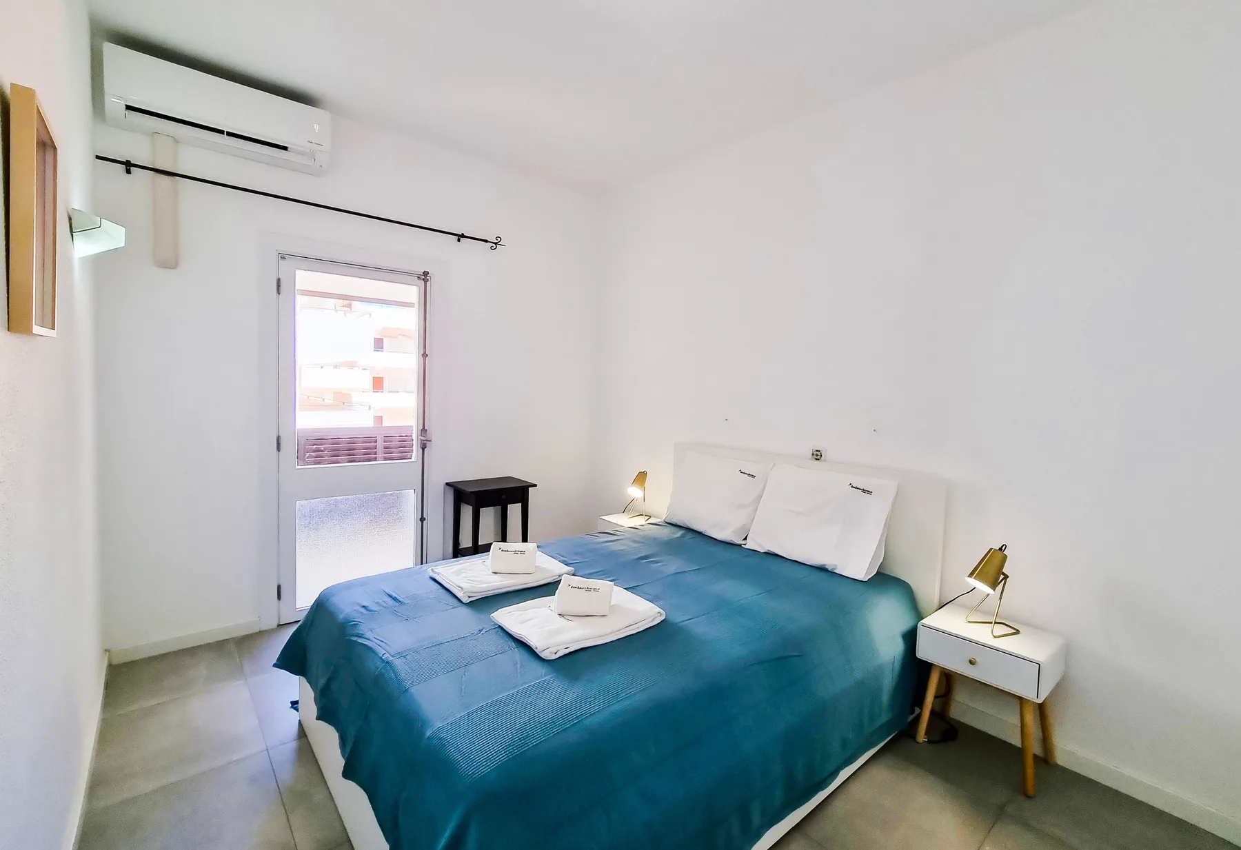 Un dormitorio con una cama cubierta con ropa de cama turquesa y una mesita de noche.