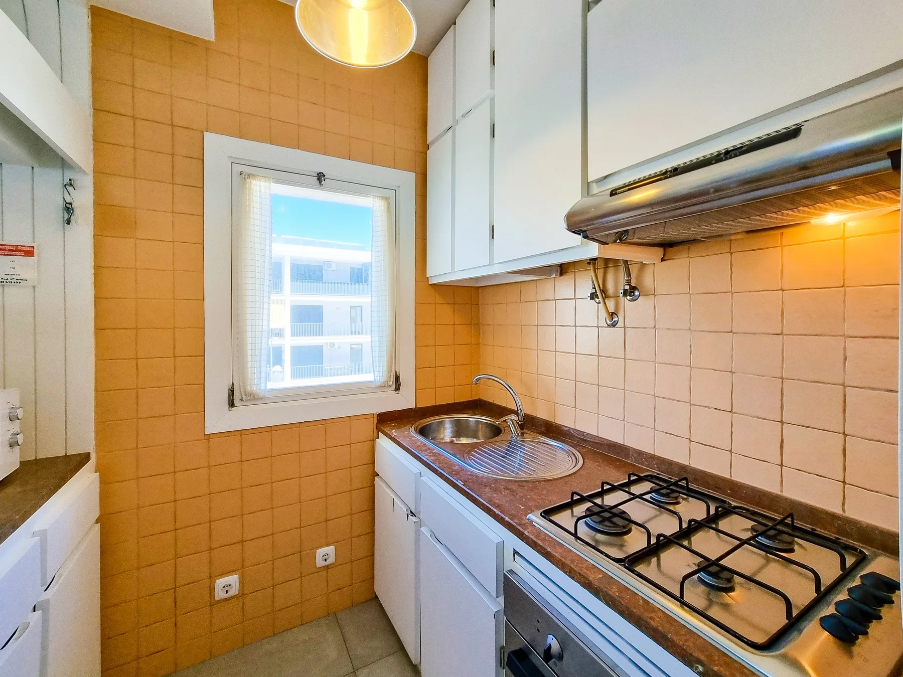 Una cocina compacta con armarios blancos y una placa de gas.