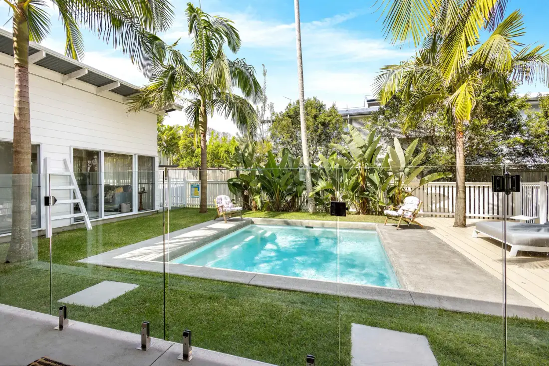 Una piscina en el patio está junto a una casa blanca y palmeras.