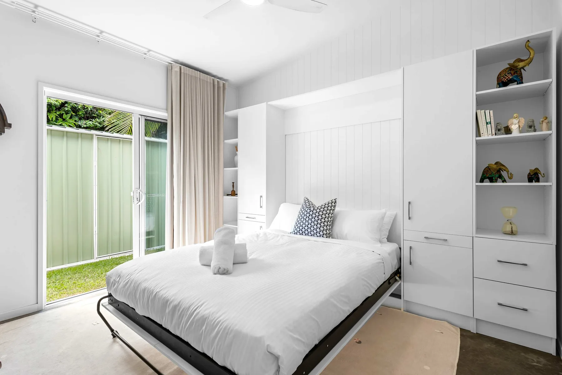 Un dormitorio luminoso con una cama tendida junto a puertas corredizas de vidrio.