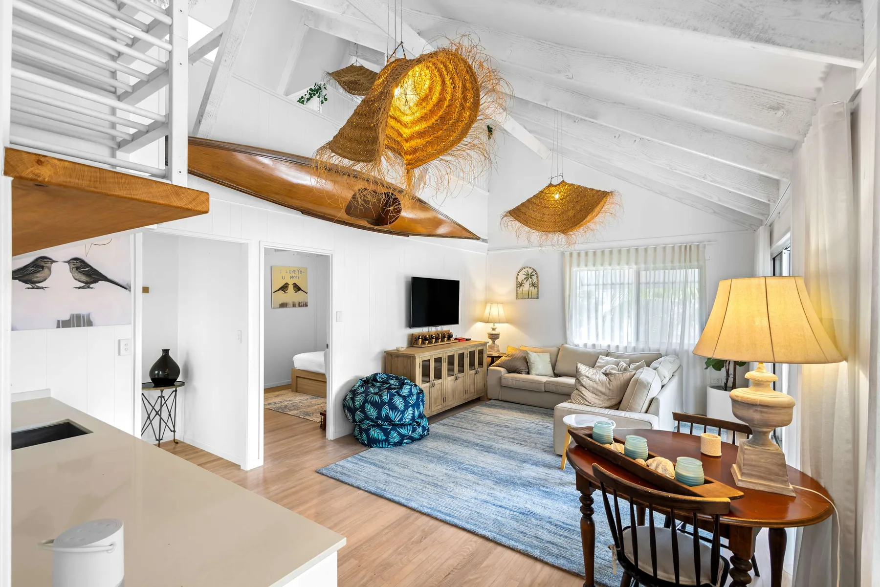 Una luminosa sala de estar de planta abierta con una barra de cocina y asientos bajo un techo blanco alto.