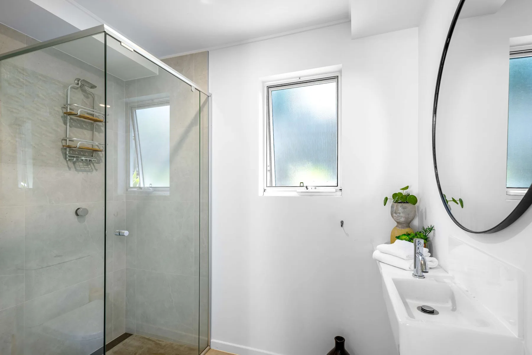 Un baño luminoso con ducha de vidrio, ventana y lavabo.