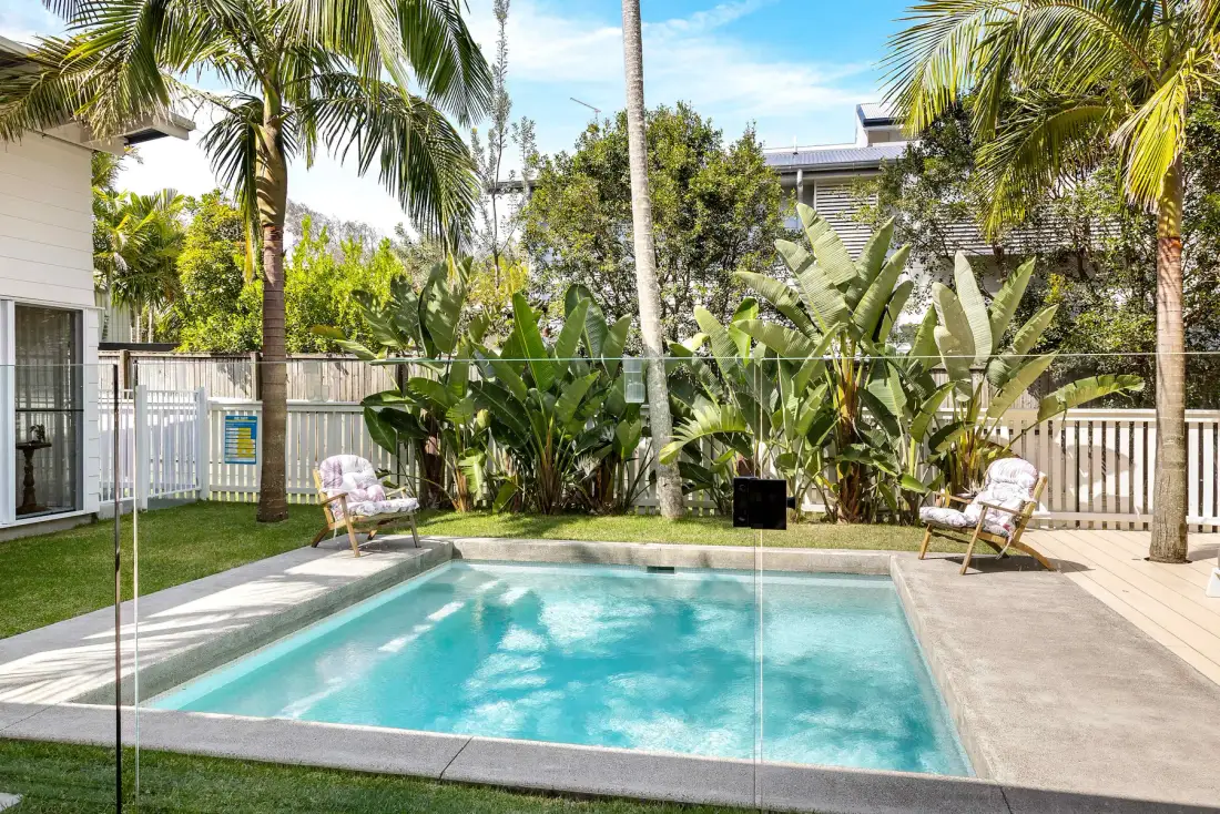 Una piscina en el patio está rodeada de plantas tropicales y asientos al aire libre.