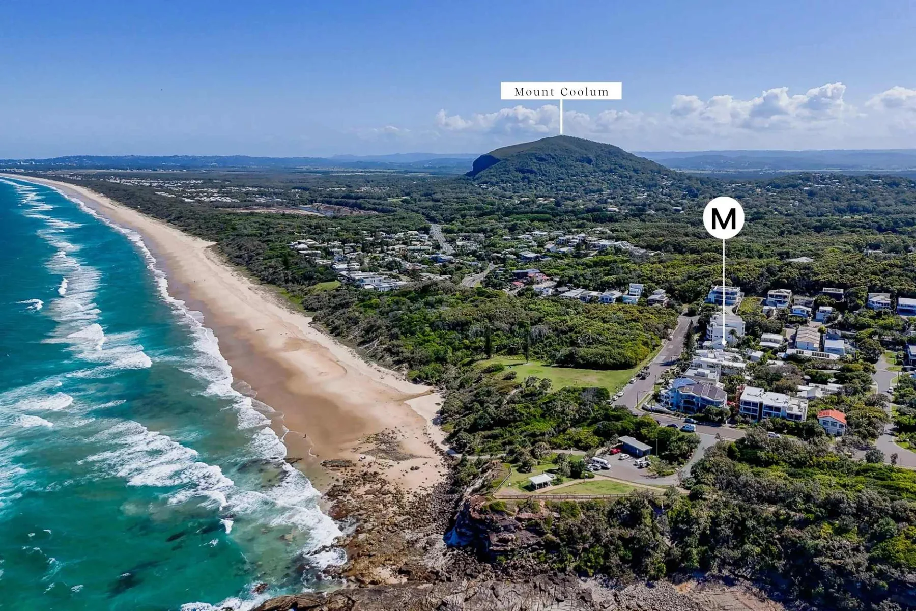 Vista aérea de una larga playa junto a viviendas costeras y vegetación verde.