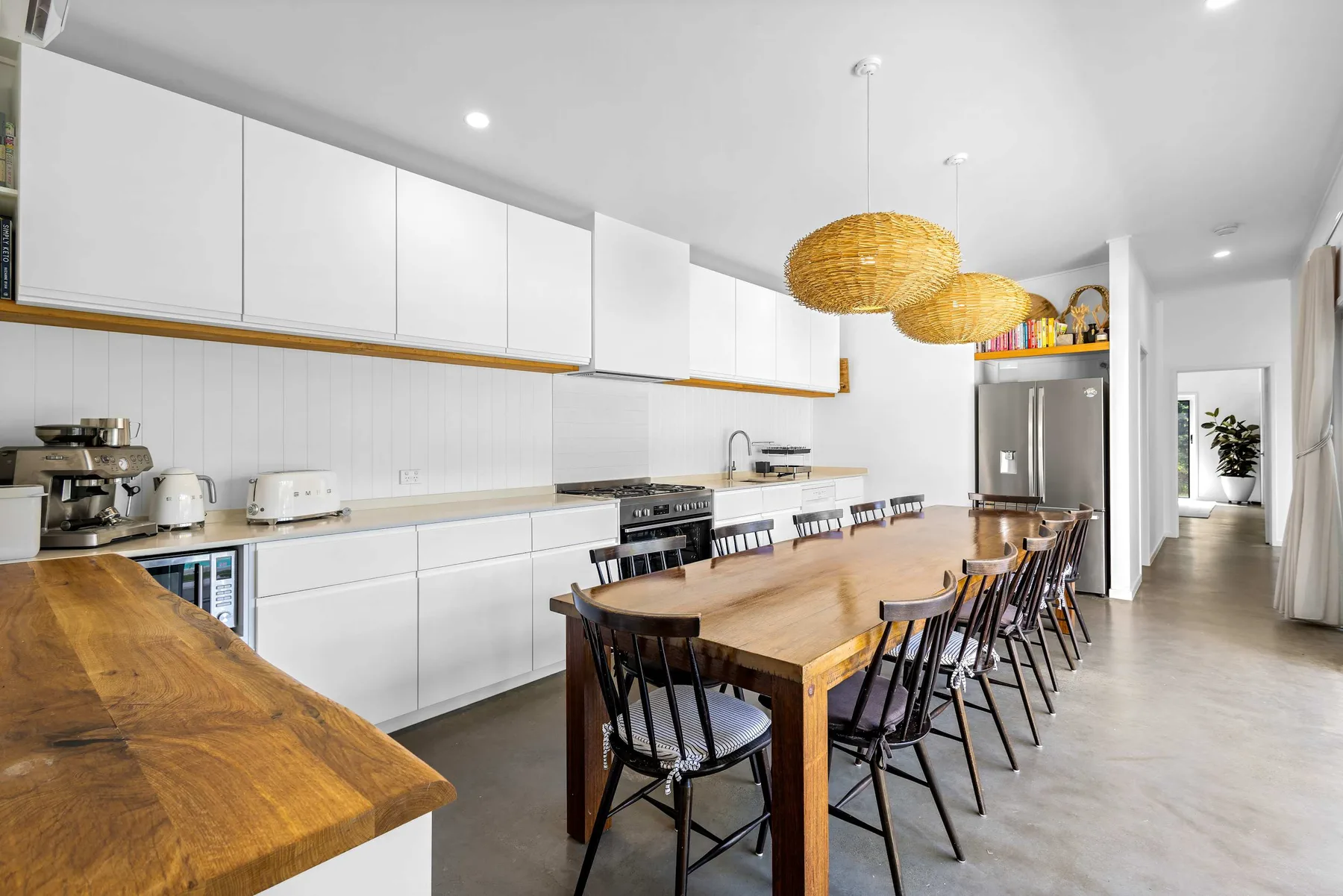 Una cocina y comedor luminosos con una mesa larga de madera y lámparas colgantes.