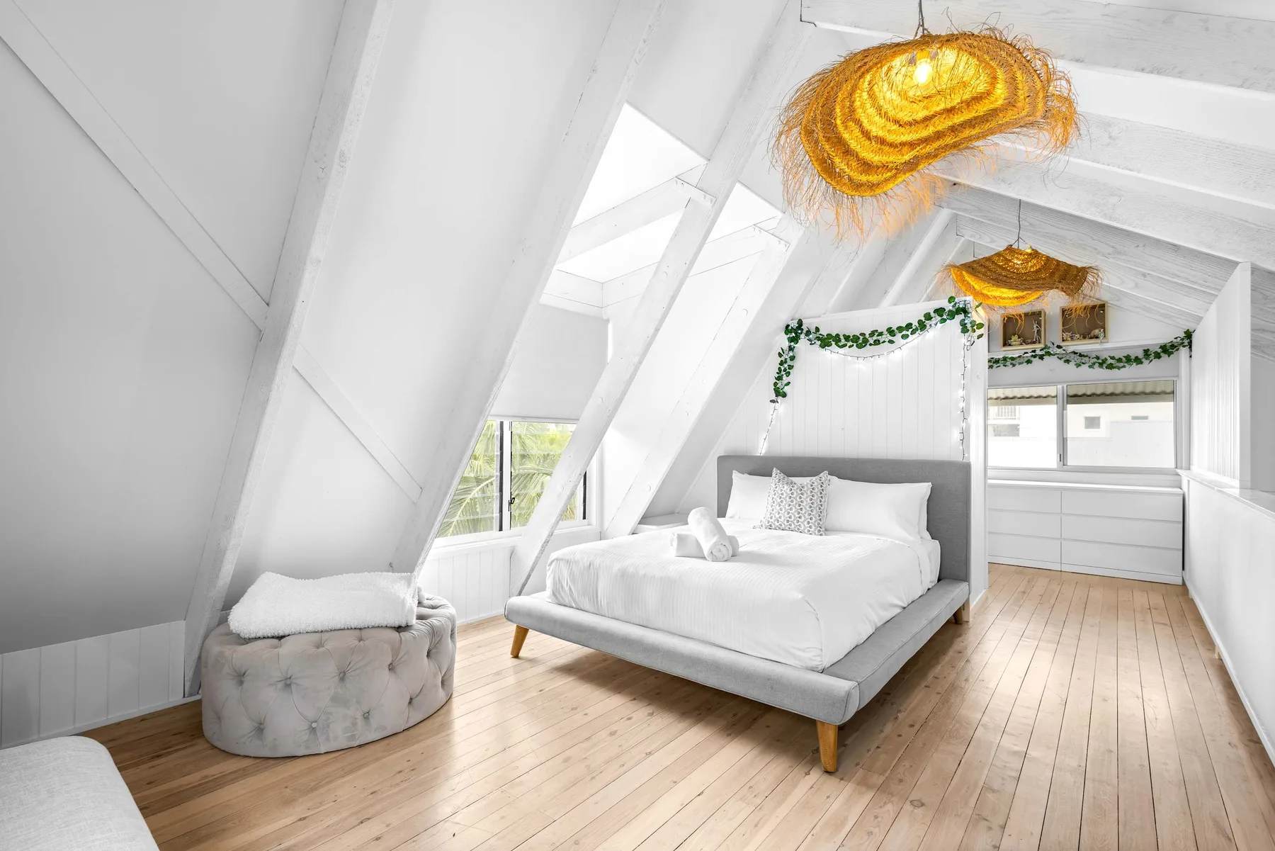 Un dormitorio abuhardillado luminoso tiene una cama bajo vigas blancas expuestas.