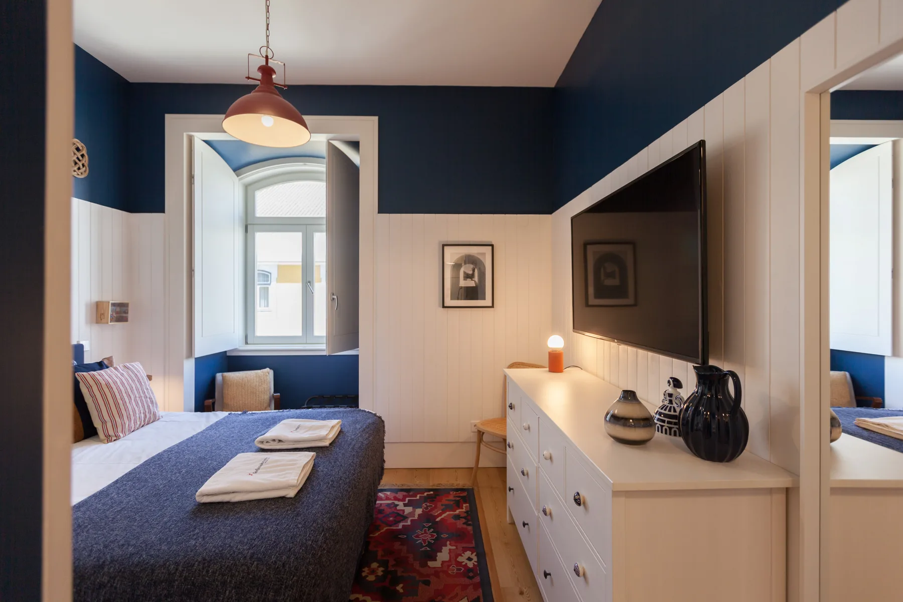 Dormitorio con una cama, un televisor y una gran ventana arqueada.