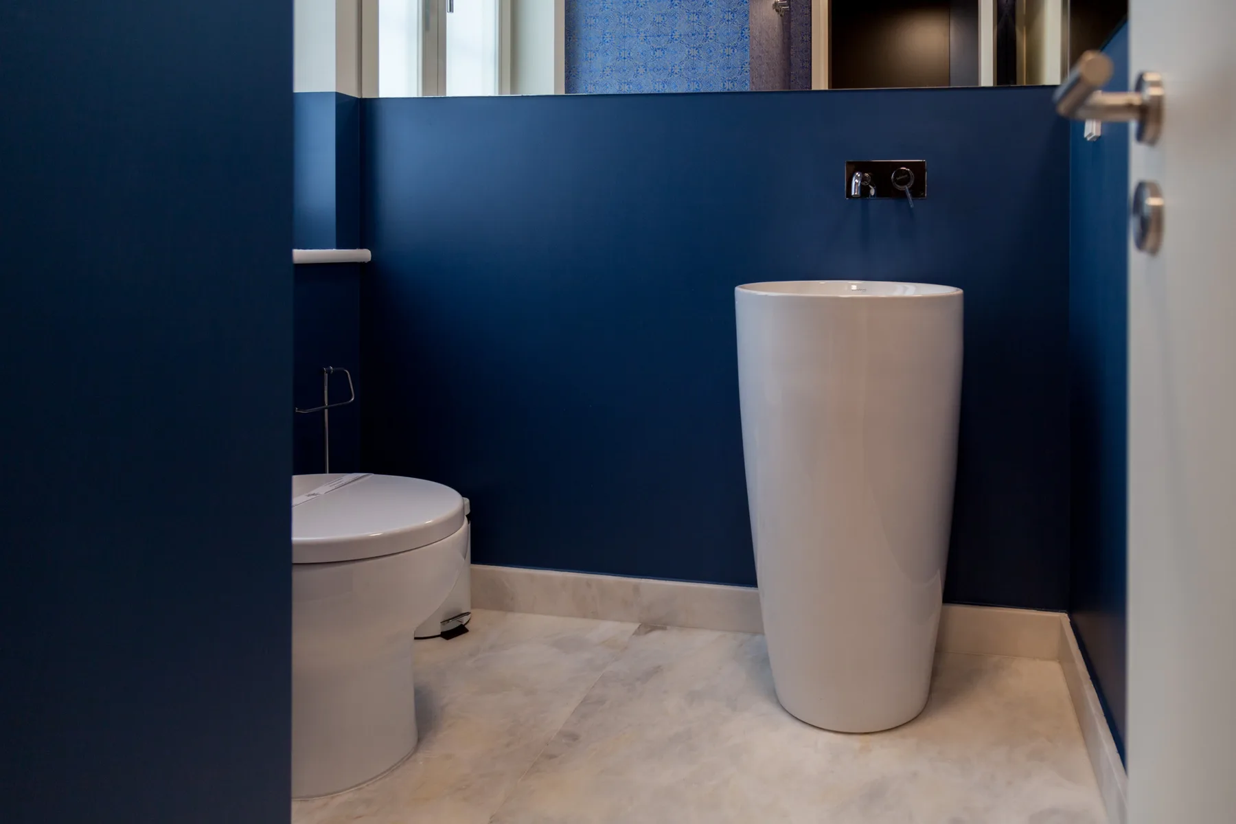 Baño con un inodoro blanco y un lavabo independiente junto a paredes azul oscuro.