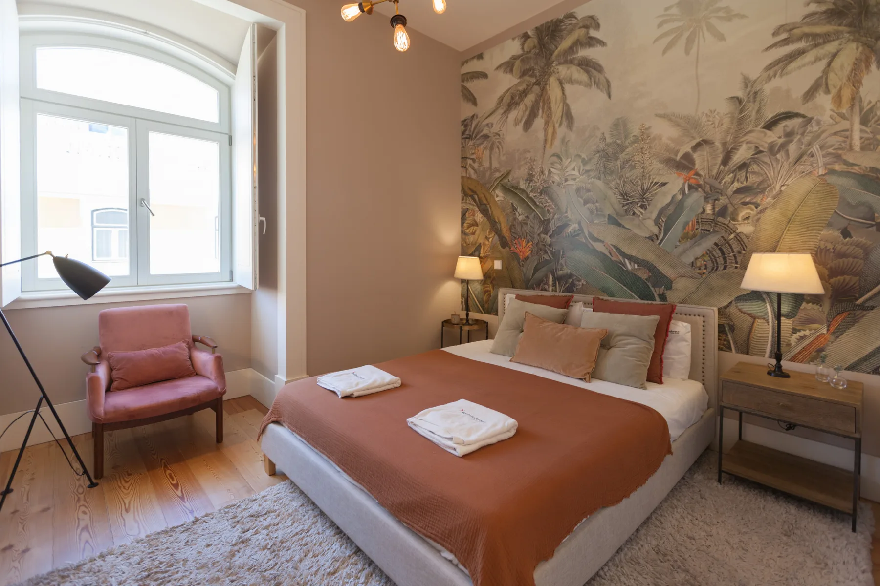 Un dormitorio con una cama vestida de tonos terracota y un mural tropical.