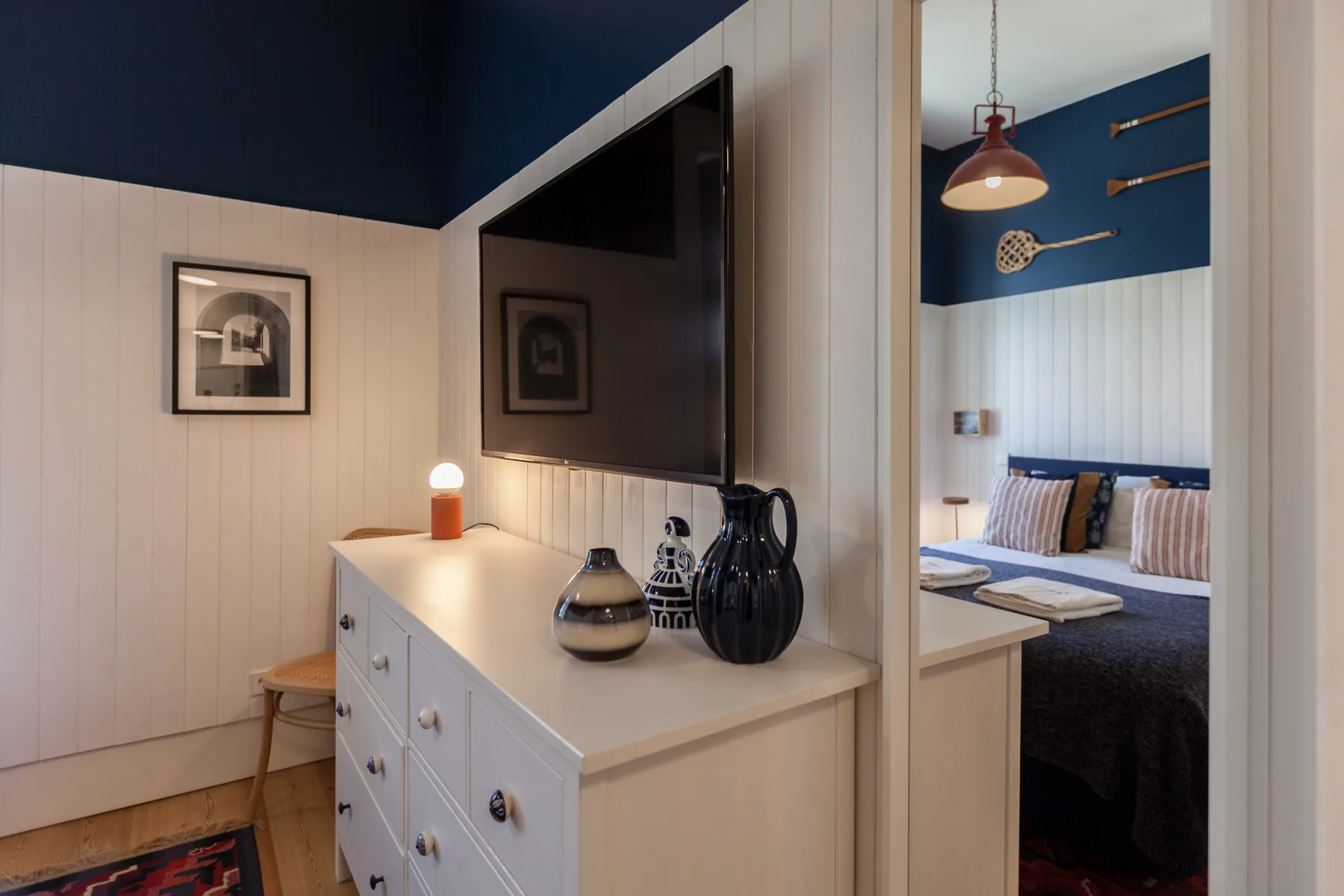 Dormitorio con una cama, un televisor montado en la pared y una cómoda blanca.