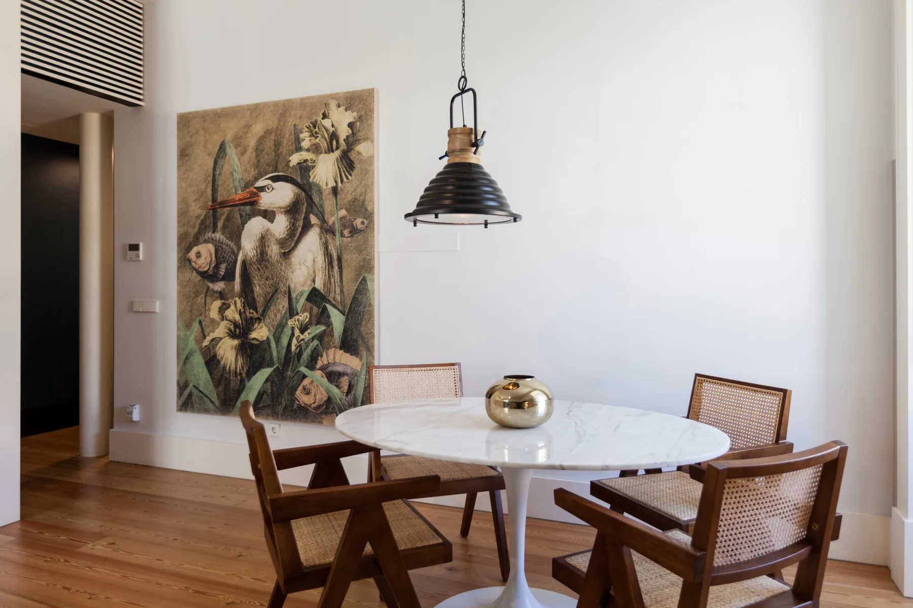 Comedor con una mesa redonda, asientos de madera y un gran cuadro en la pared.