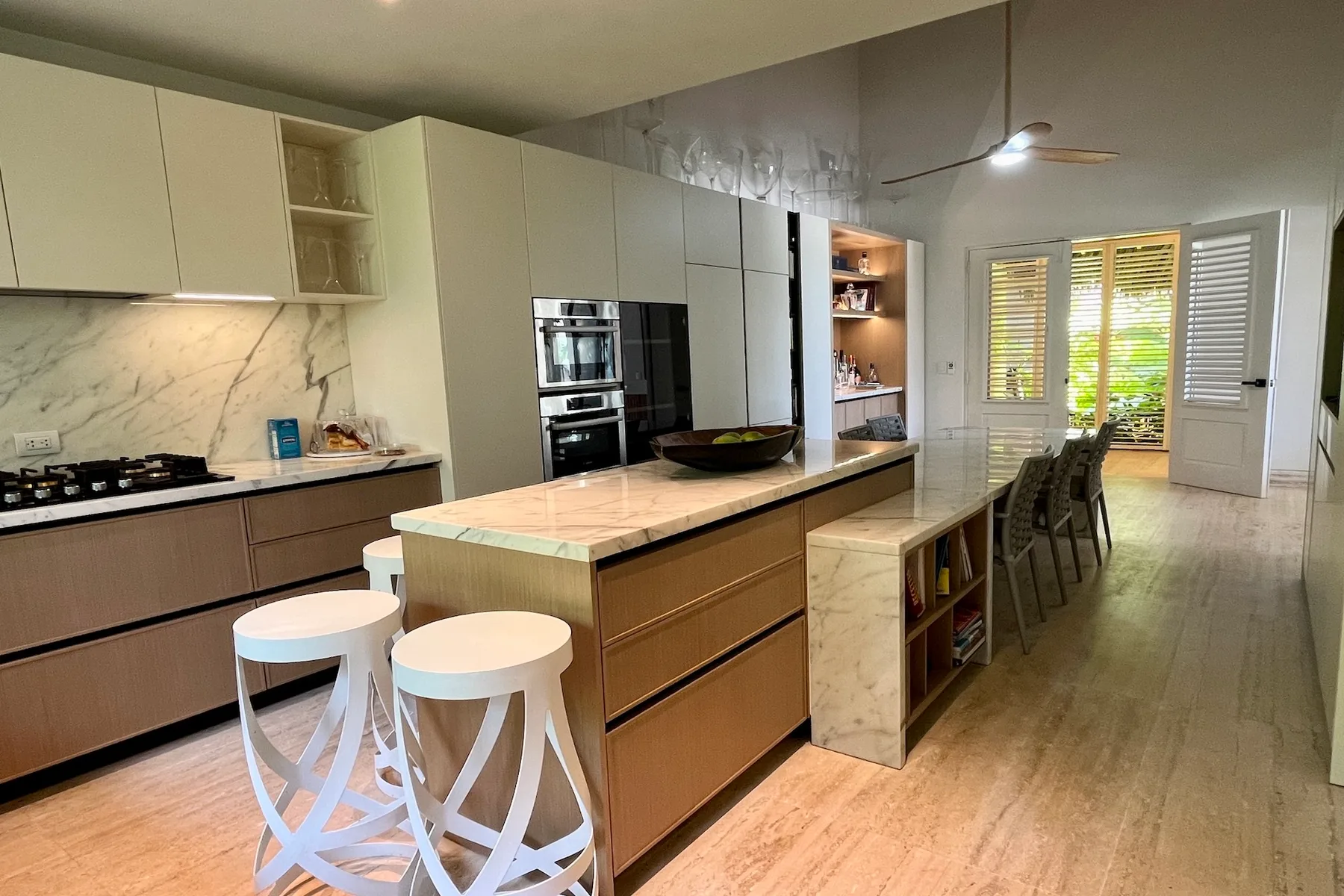 Una cocina luminosa con una isla central, asientos de barra y una mesa de comedor junto a las ventanas.