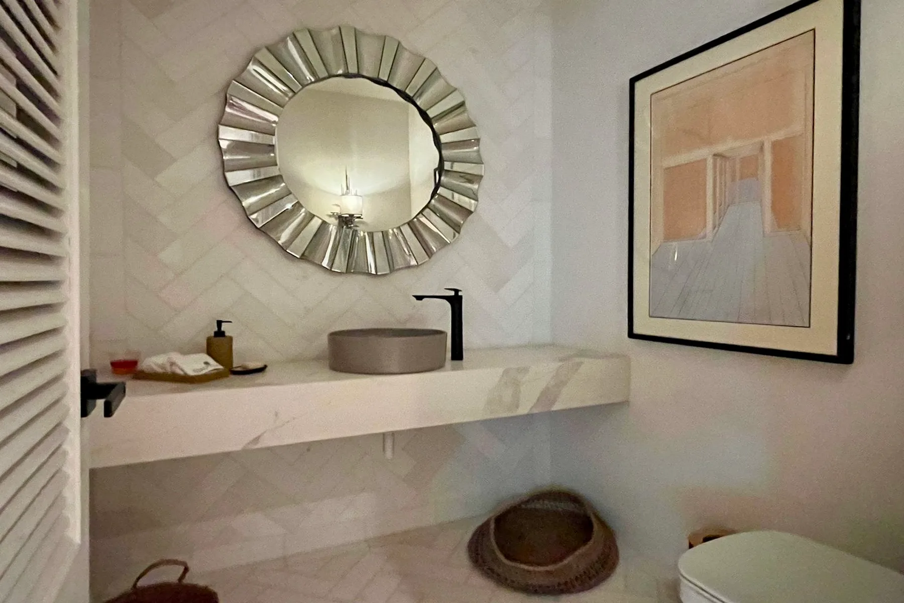 Un tocador de baño con lavabo de recipiente, espejo redondo y obra enmarcada.