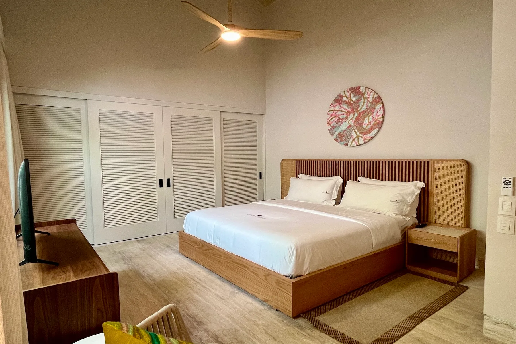 Un dormitorio con una cama bien tendida, puertas de armario con persianas y un ventilador de techo.