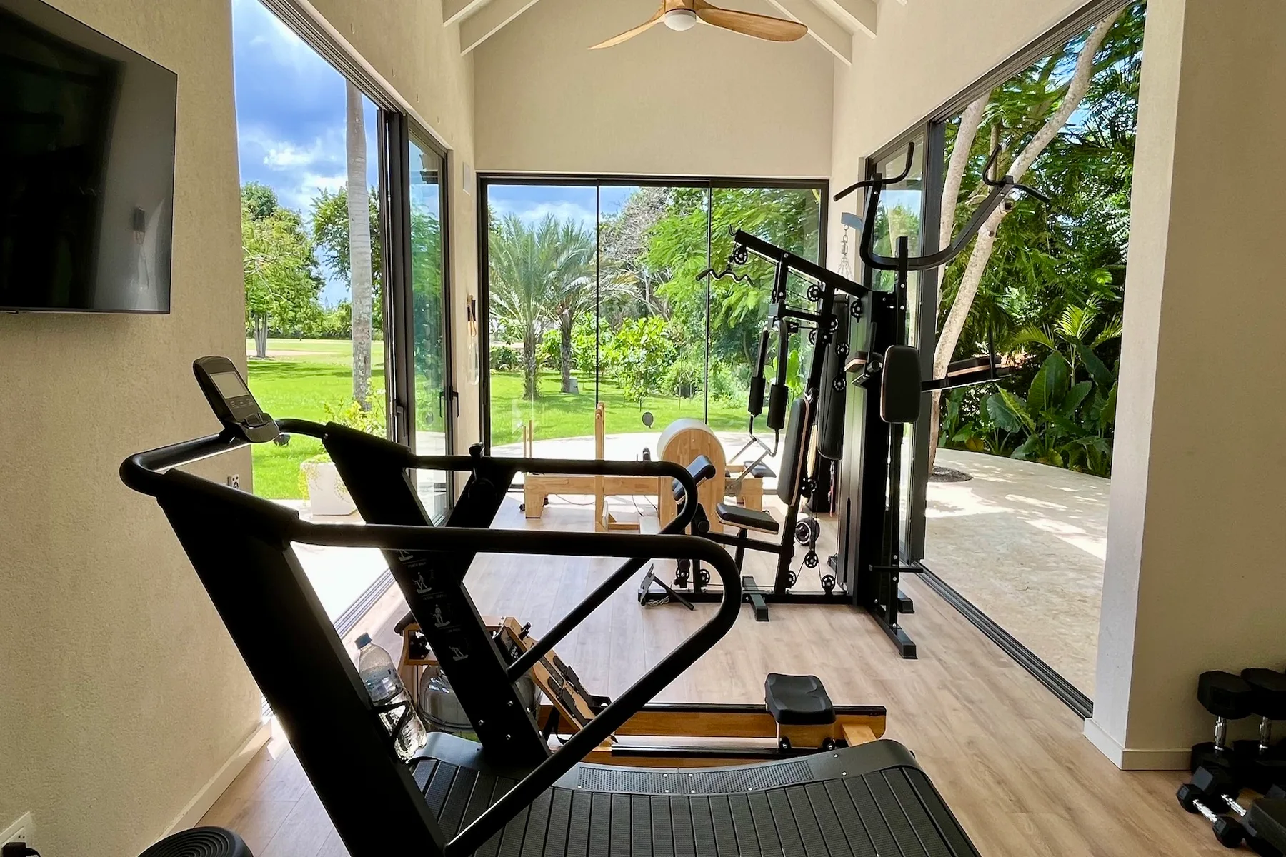 Un gimnasio luminoso con máquinas de ejercicio junto a grandes ventanas que dan a zonas verdes.