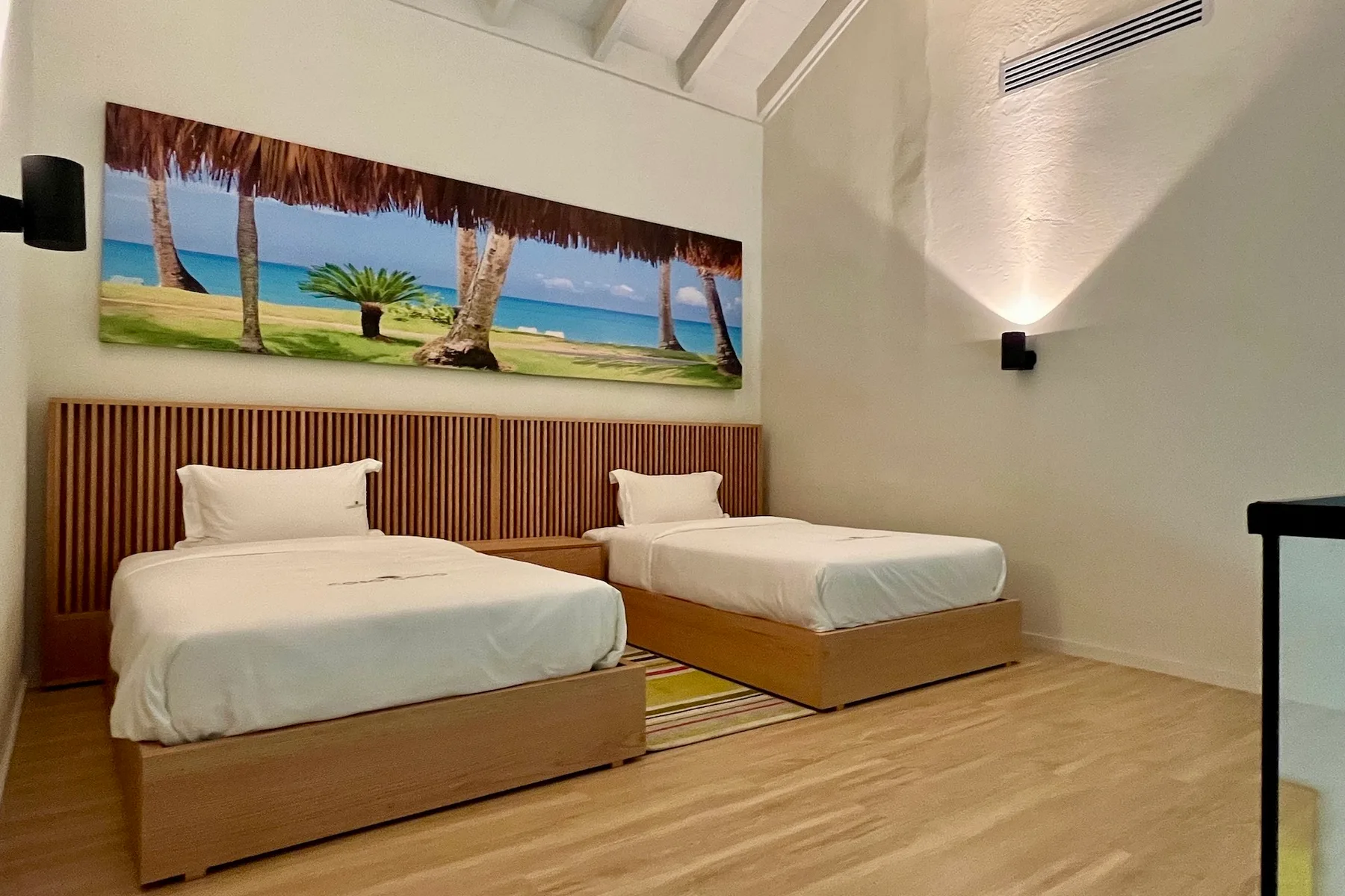 Un dormitorio con dos camas y una gran imagen de una playa tropical en la pared.