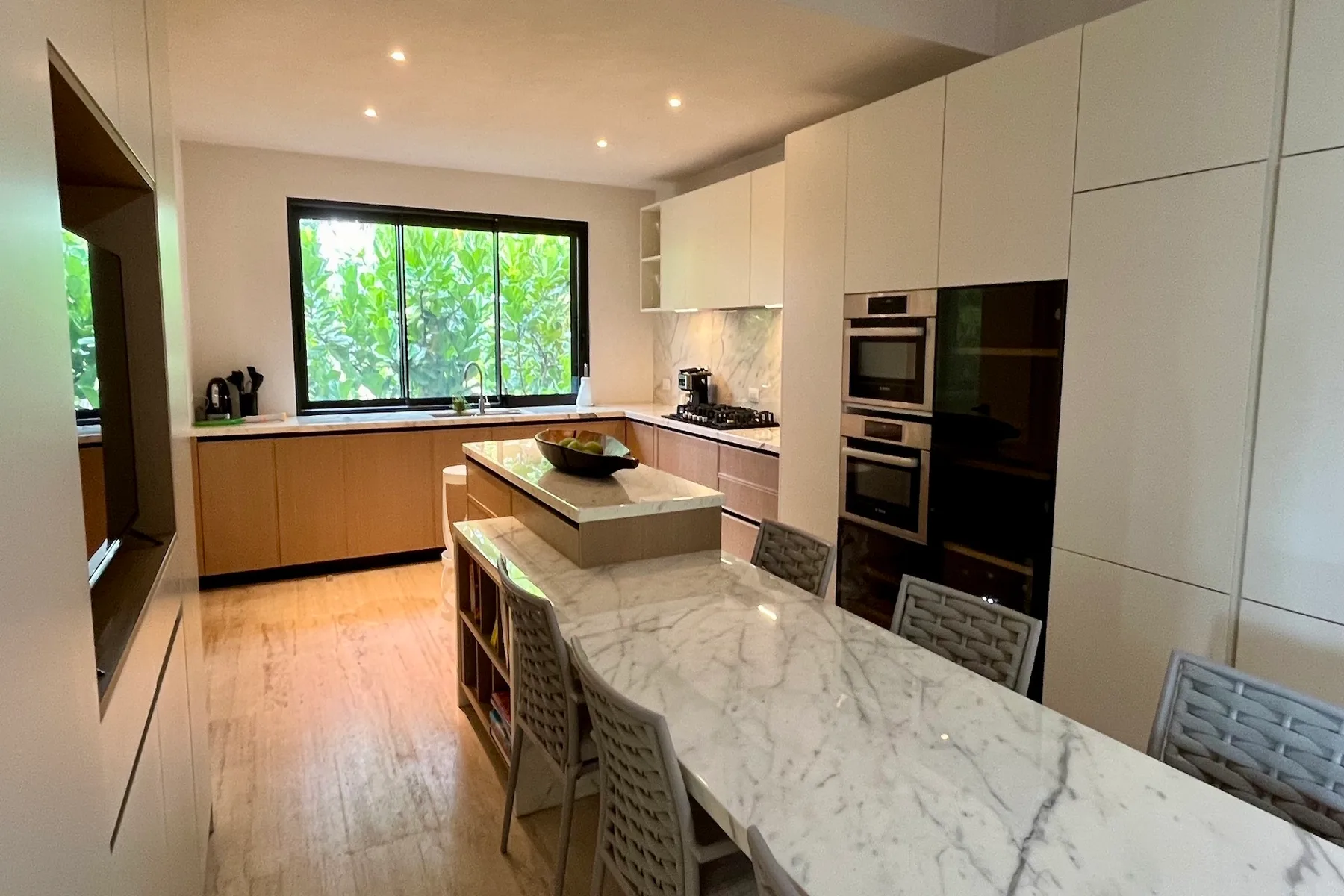 Una cocina moderna y luminosa con una isla de mármol y una gran ventana con vistas a la vegetación.
