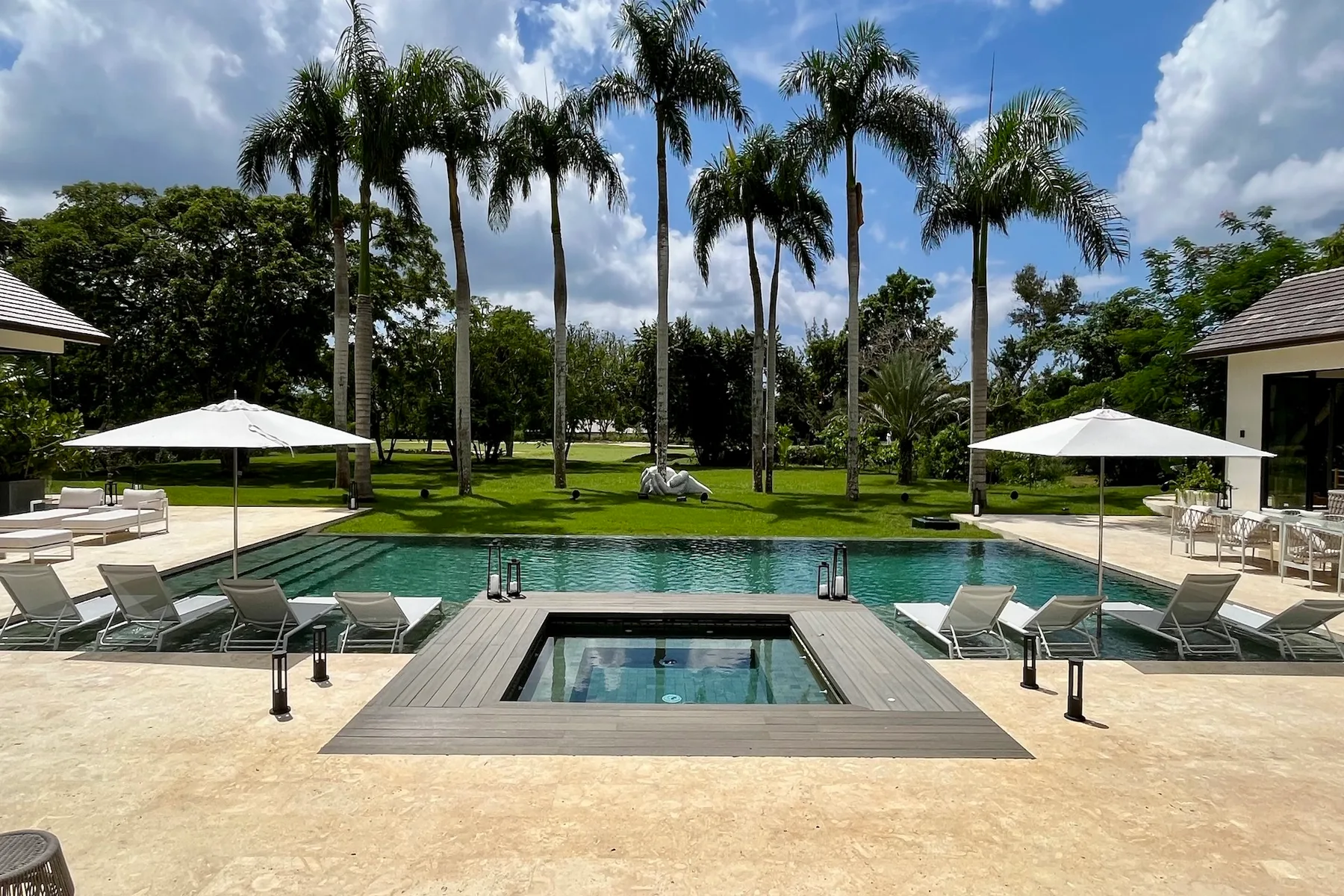 Una piscina exterior y un spa están rodeados de palmeras y asientos de descanso.