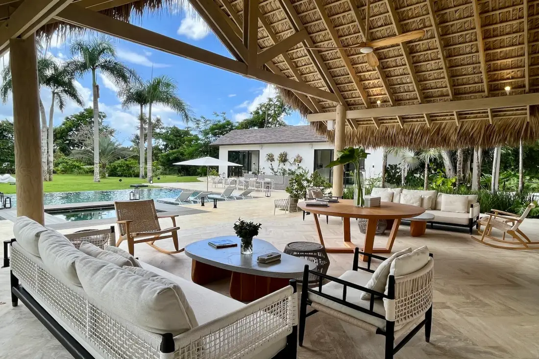 Una sala al aire libre y zona de comedor dan a una piscina y jardines.