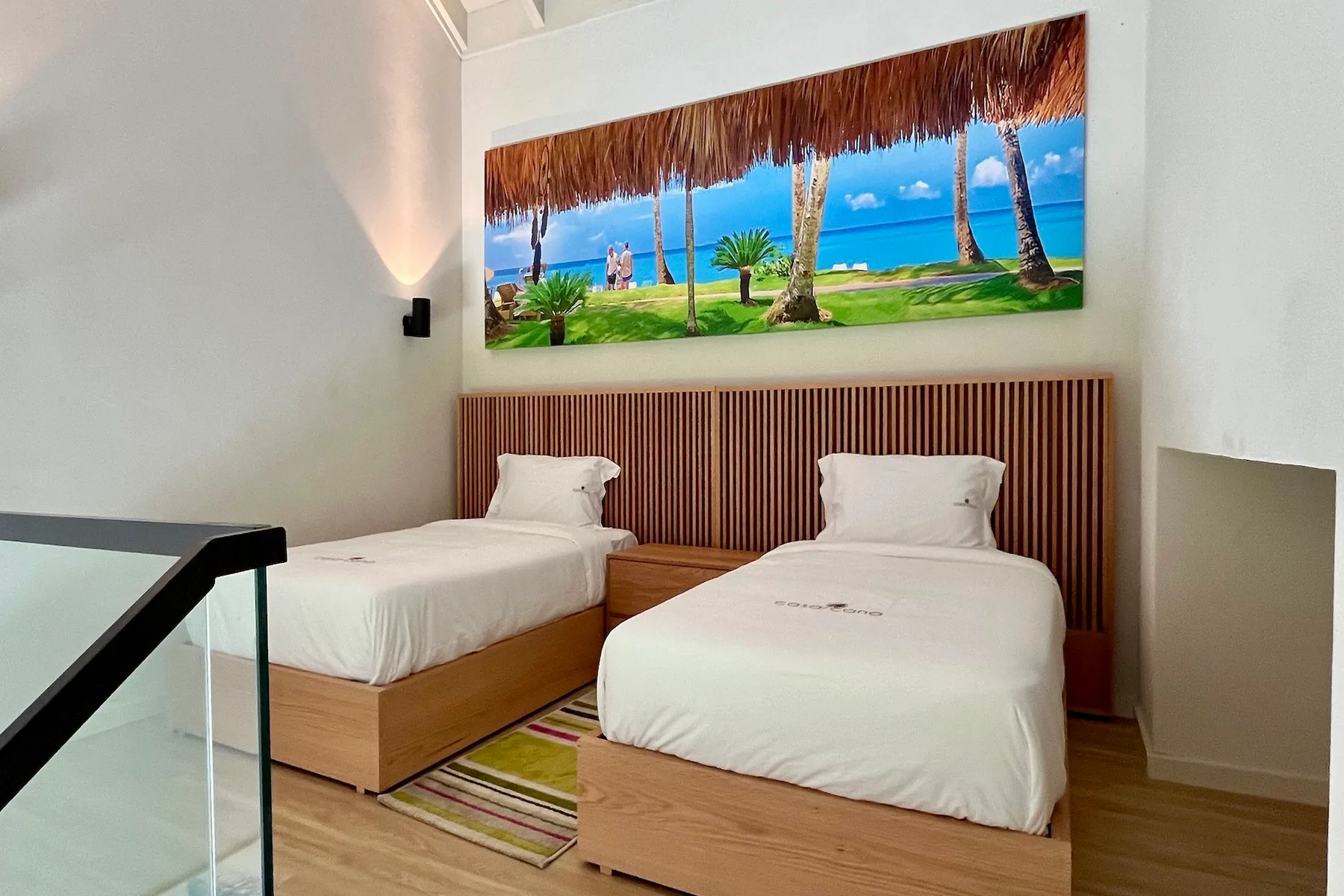 Un dormitorio con dos camas y una colorida escena de playa sobre el cabecero.