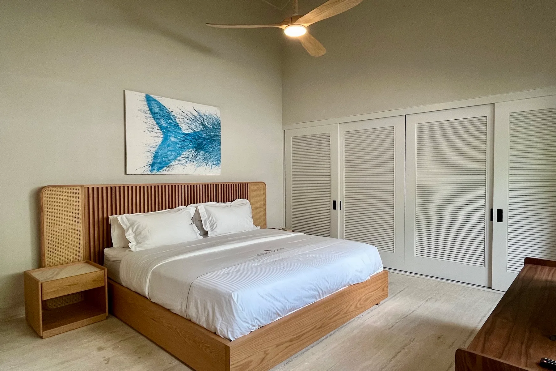 Un dormitorio con una cama bien tendida y puertas blancas de armario con persianas.