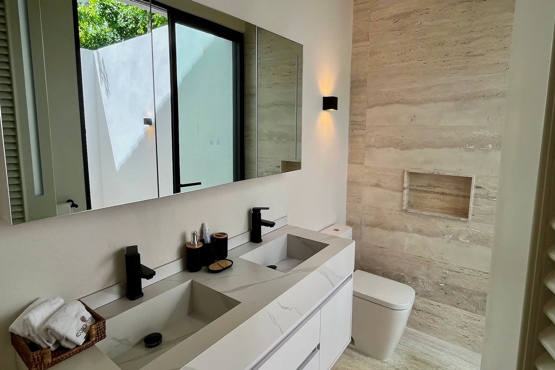 Un tocador de baño con dos lavabos y un inodoro junto a una pared de piedra.