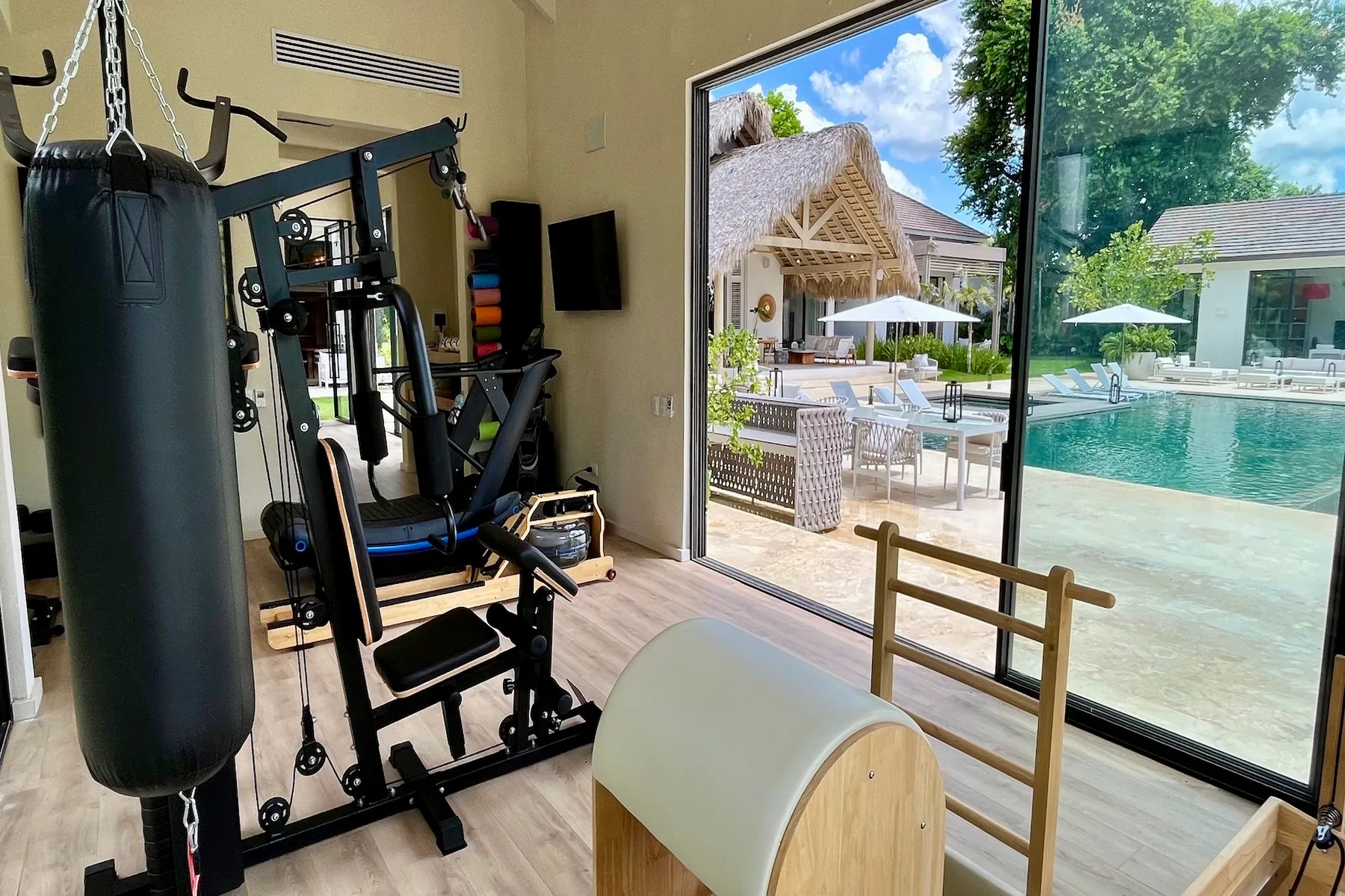 Un gimnasio con equipo de ejercicio da a una piscina exterior y un patio.